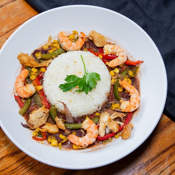 Haitian dish with white rice, shrimp, chicken, corn, red peppers, and green beans in a rich sauce.