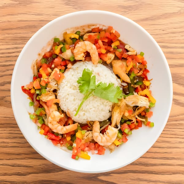 Haitian dish with white rice, shrimp, chicken, and colorful diced vegetables in a white bowl.