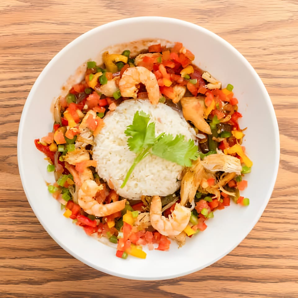 Haitian dish with white rice, shrimp, chicken, and colorful diced vegetables in a white bowl.