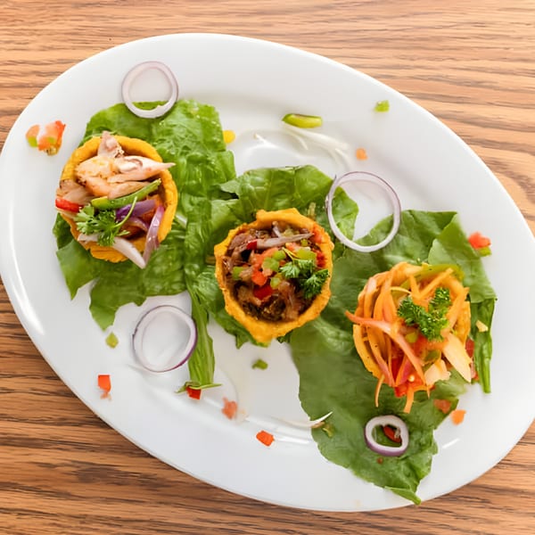 Three Haitian plantain cups filled with meat and vegetables, garnished with lettuce and onion rings.