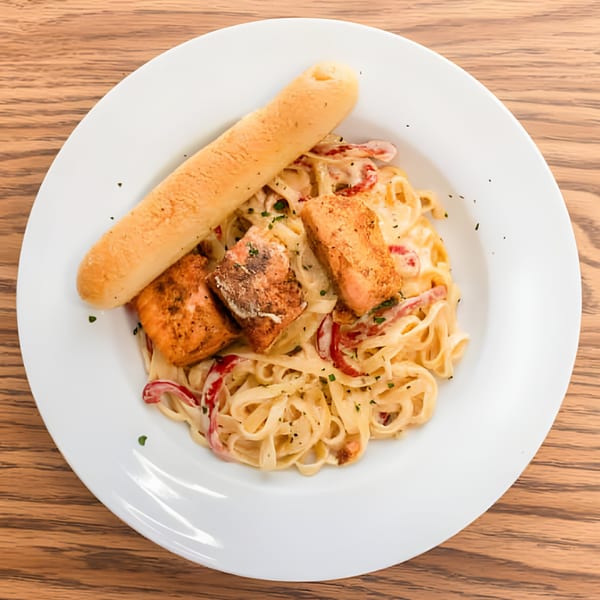 Haitian salmon pasta with red peppers and a breadstick on a white plate.