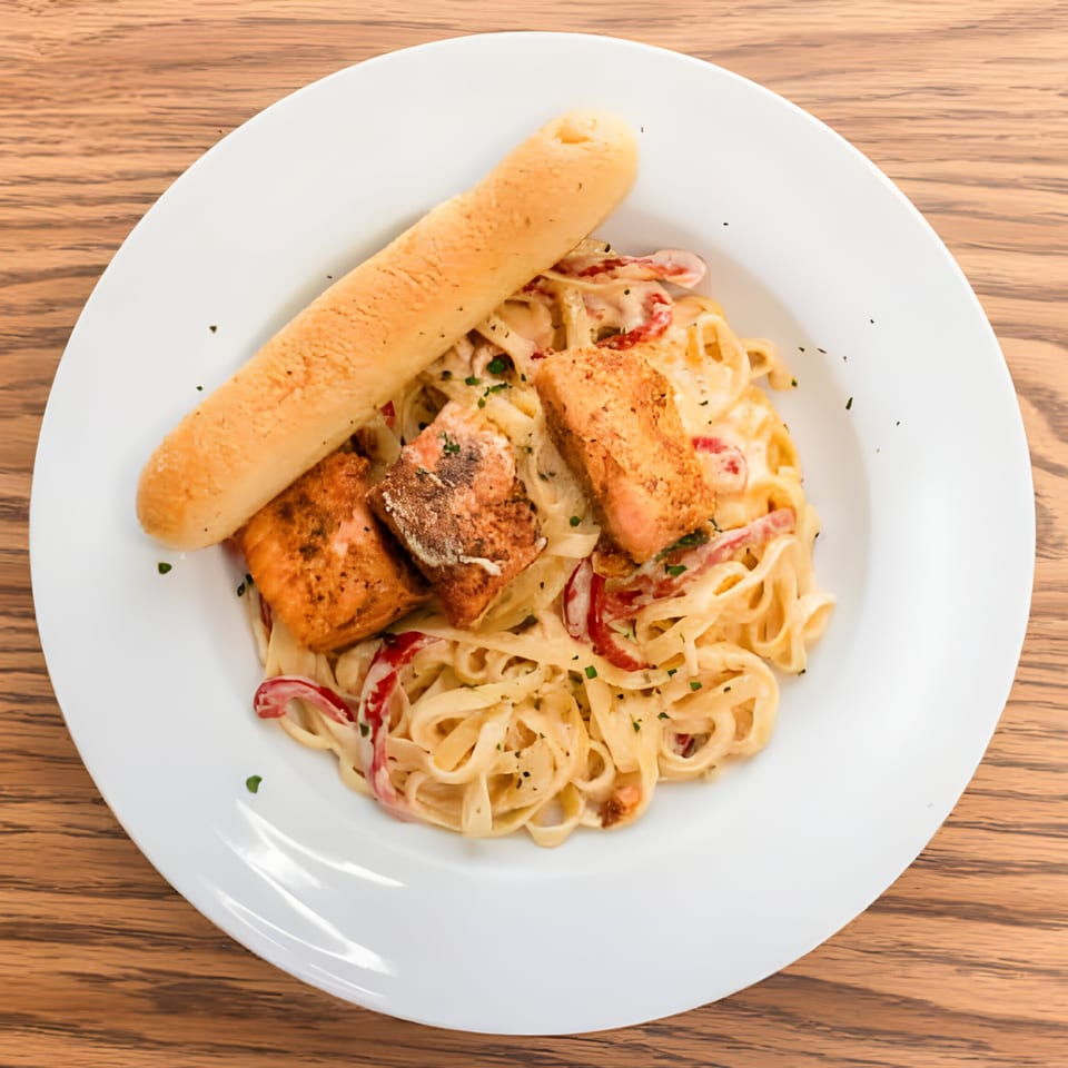 Haitian salmon pasta with red peppers and a breadstick on a white plate.