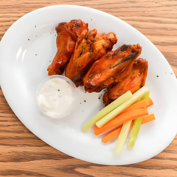 Le Boulevard Bar & Grills' chicken wings with dipping sauce, celery, and carrot sticks on a white plate.