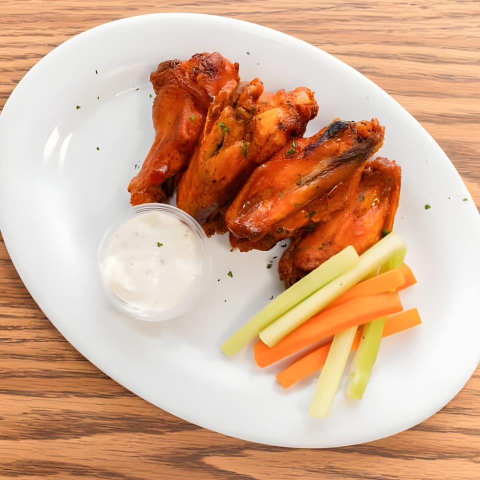 Le Boulevard Bar & Grills' chicken wings with dipping sauce, celery, and carrot sticks on a white plate.
