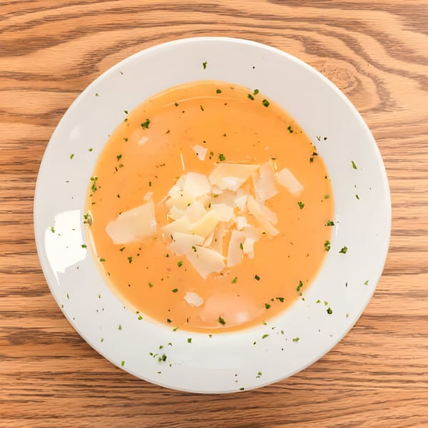 Haitian pumpkin soup, Joumou, with shaved parmesan and parsley on a white plate.