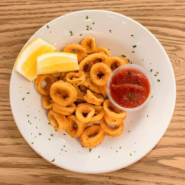 Golden fried calamari rings with lemon wedges and a side of red dipping sauce on a white plate.